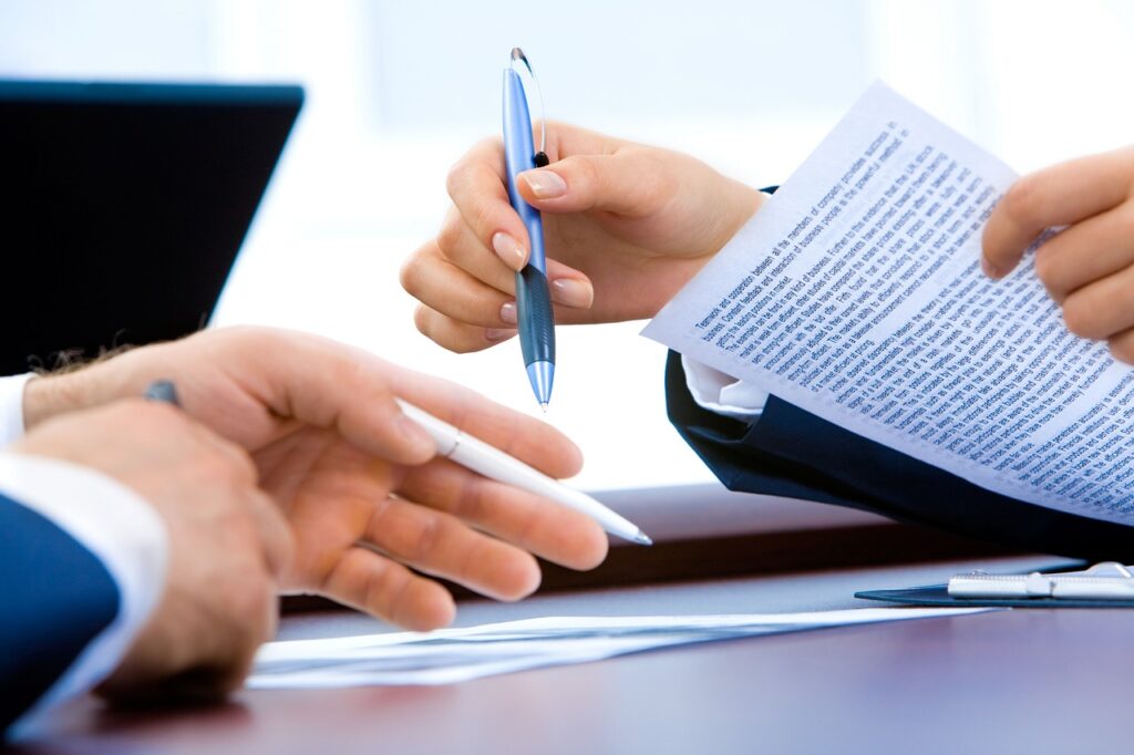Hands of professionals reviewing and discussing a printed document, holding pens, in a business meeting setting.