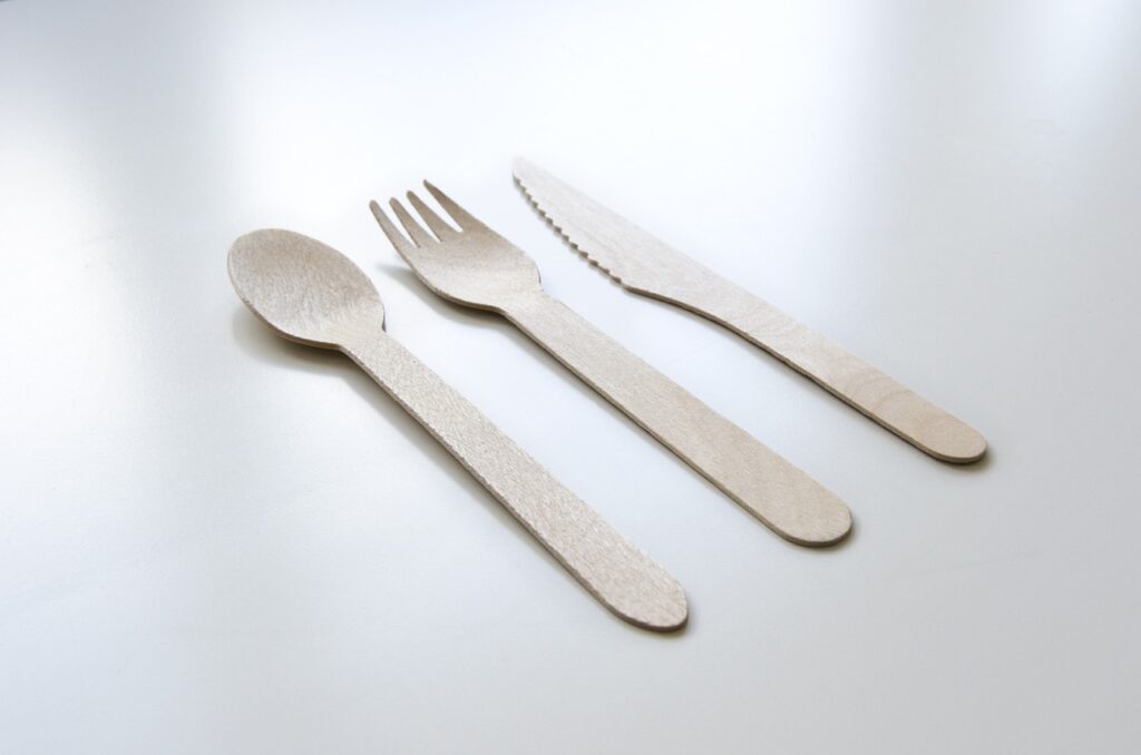 A set of three wooden utensils—spoon, fork, and knife—placed side by side on a white surface.