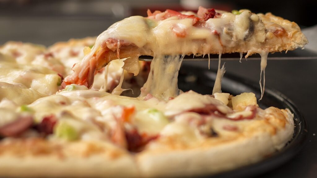 Close-up of a slice of cheese-loaded pizza being lifted from a full pizza, with melted cheese stretching from the pan.