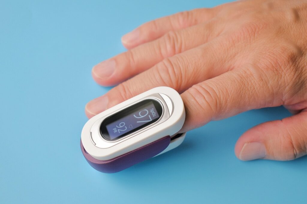 A fingertip pulse oximeter clipped onto a person's index finger, displaying oxygen saturation and pulse rate readings.