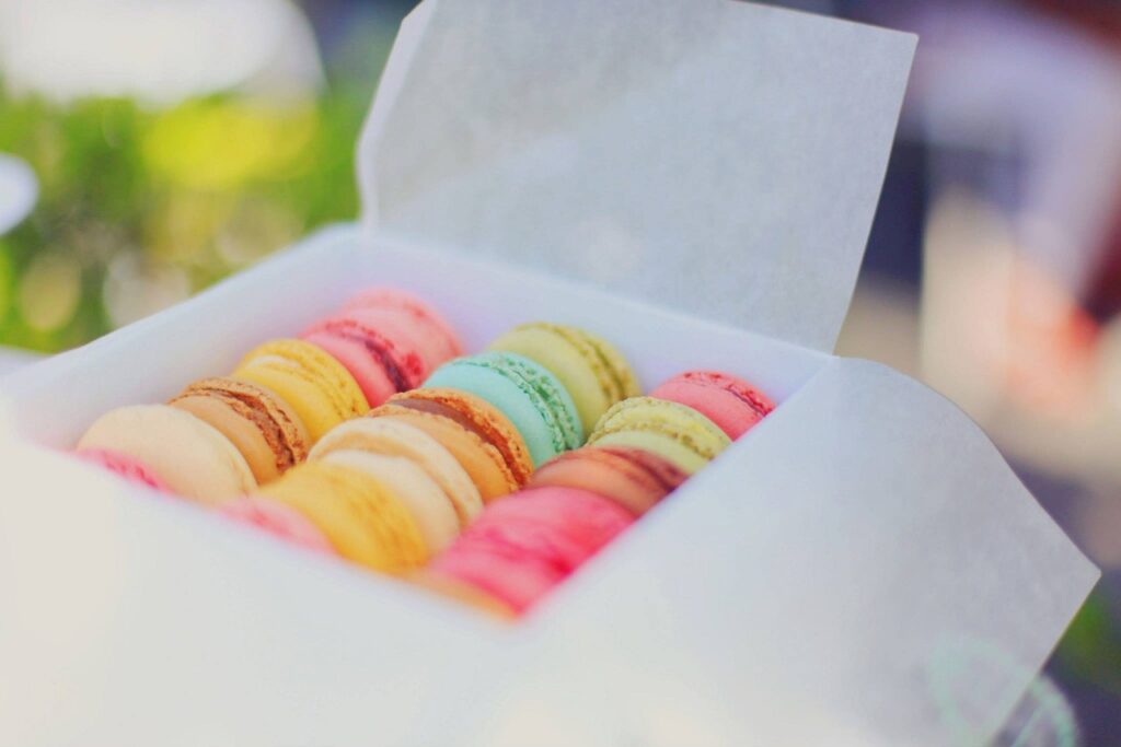Box of assorted colorful macarons neatly arranged in rows, with hues including pink, yellow, green, and blue.