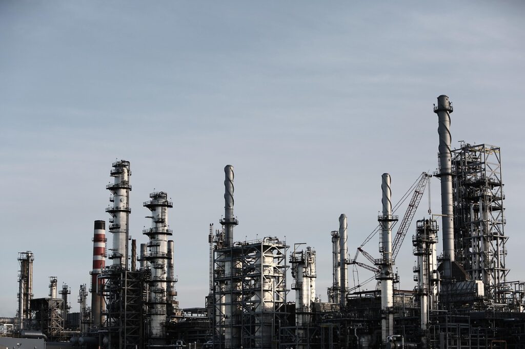 Petrochemical refinery with multiple tall distillation towers, pipes, and industrial cranes under a clear sky.