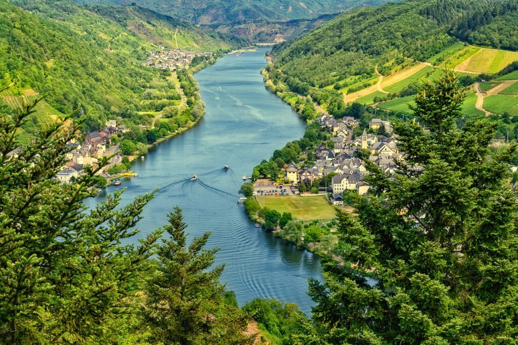 Aerial view of a river flowing through a green valley with villages on both sides, surrounded by forested hills and farmland.