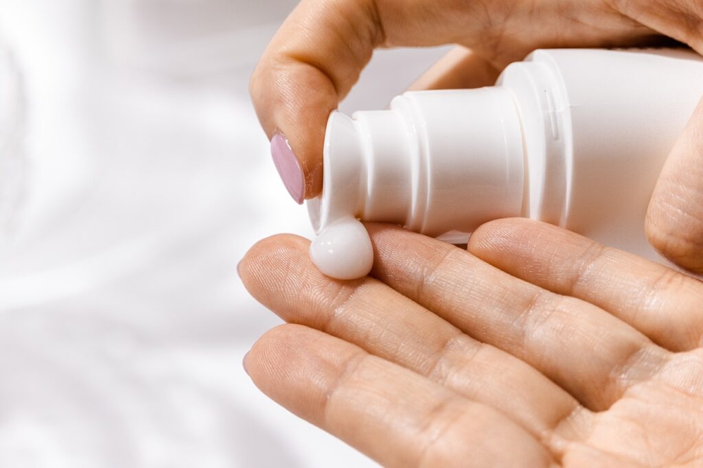 Close-up of a person dispensing white lotion or cream from a pump bottle onto their hand.