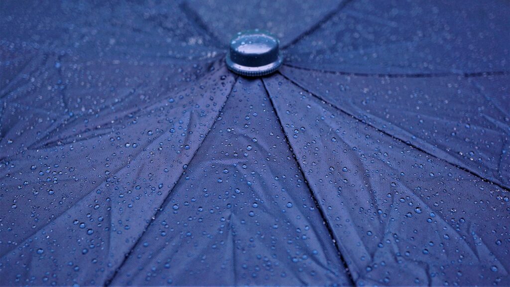 Close-up view of water droplets beading on a dark blue umbrella surface, showing water resistance.