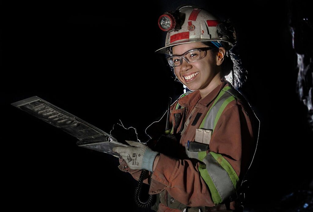 Smiling geologist or mining technician in protective gear holding a rock core sample tray underground.