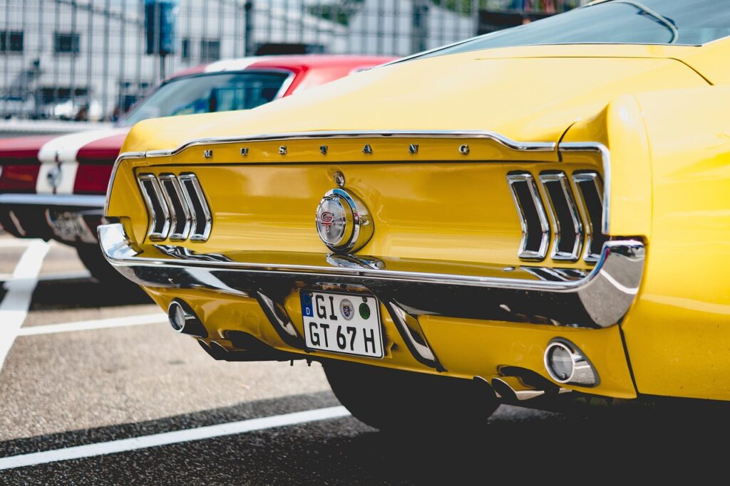 Rear view of a bright yellow classic Ford Mustang GT with chrome detailing and a European license plate.
