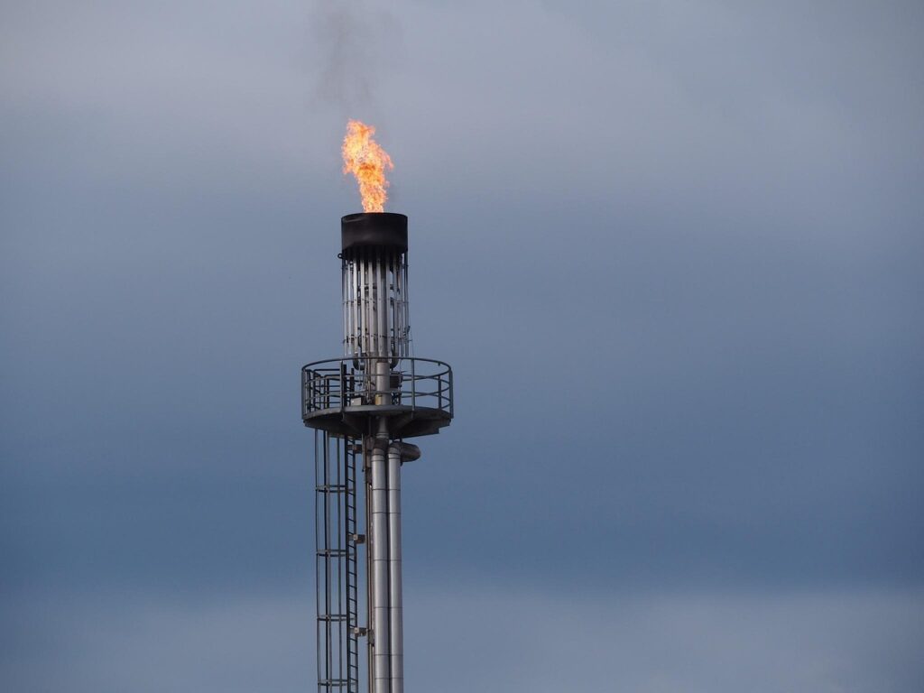Industrial flare stack burning off excess gas against a cloudy sky in an oil and gas facility.