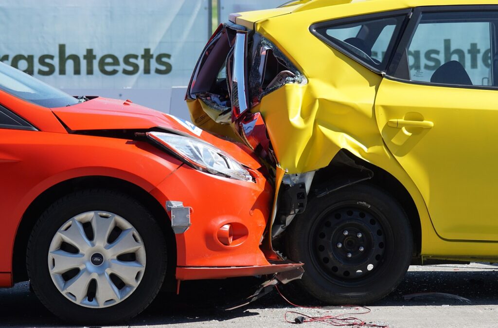 Frontal crash test showing a red car colliding with the rear of a yellow car, both visibly damaged.