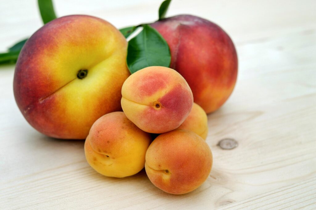 Fresh peaches and apricots with leaves arranged on a light wooden surface.