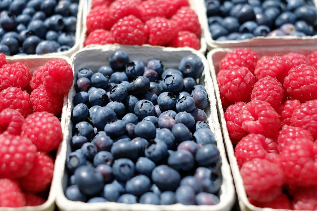 Close-up of fresh blueberries and raspberries in paper cartons, arranged in a market-style display.