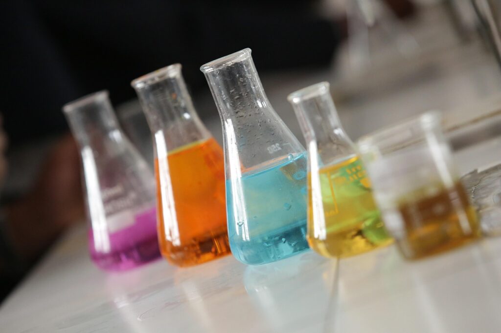 Colorful liquids in a row of laboratory Erlenmeyer flasks and beakers on a white countertop.