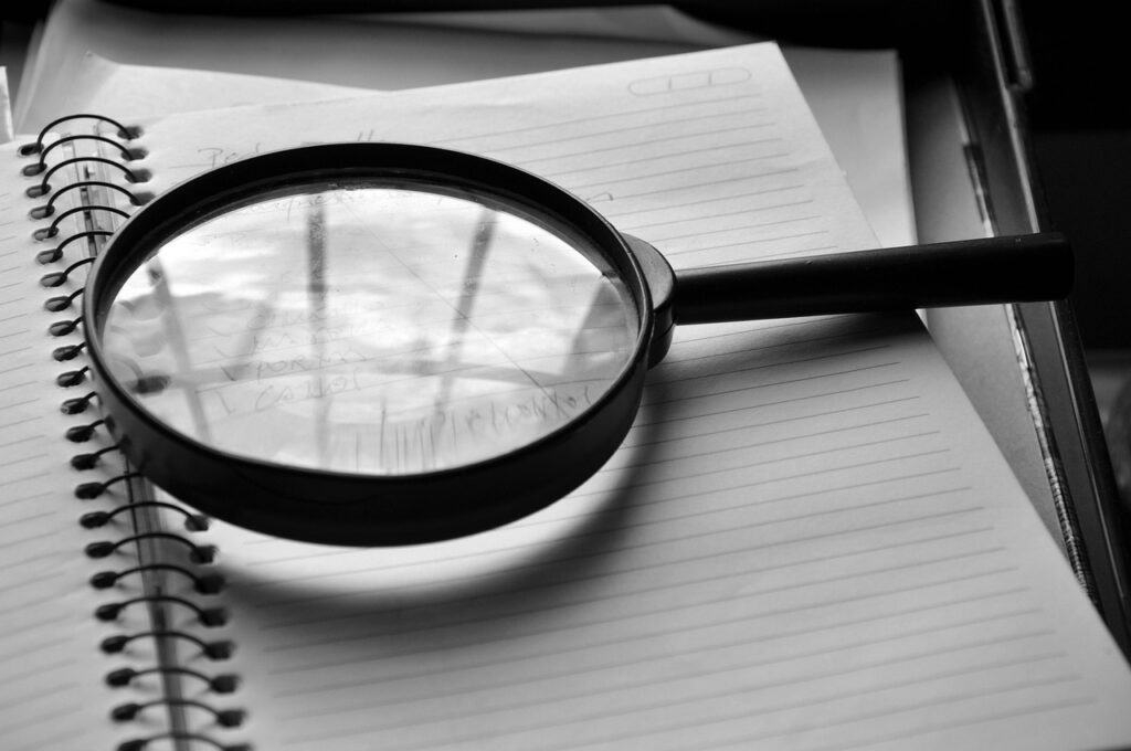 Black-and-white photo of a magnifying glass resting on an open spiral notebook with lined pages.