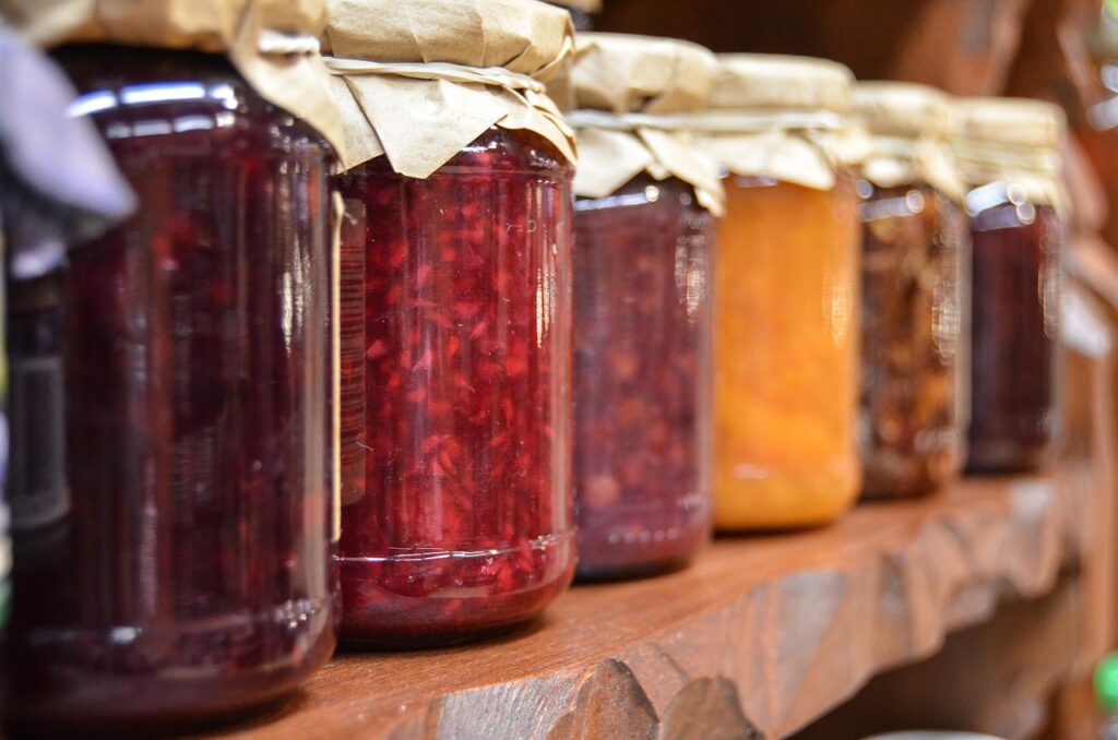 Close-up view of assorted glass jars filled with colorful preserves and jams, lined up on a wooden shelf.
