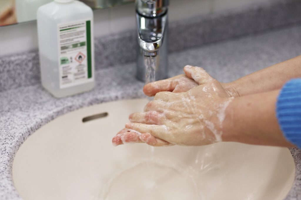 Person washing their hands with soap under running water at a sink, with a disinfectant bottle in the background.