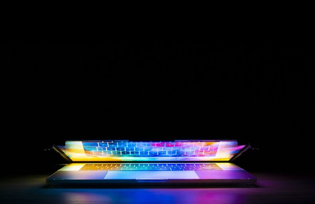 A partially closed laptop glowing with vibrant rainbow-colored light in a dark room.