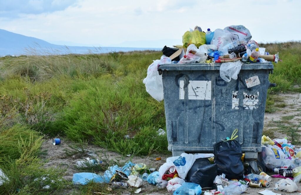 a dumpster overflowing with garbage sitting ina green field illustrating the importance of testing for persistent organic pollutants in the environment