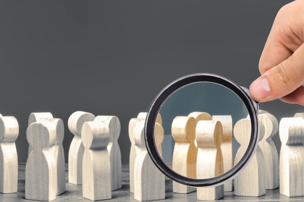 Magnifying glass held up to wooden figures to denote the new sharing of clinical data standards