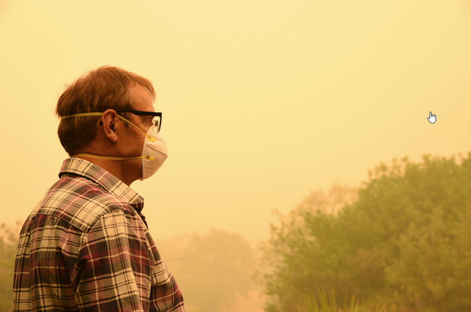 Man wearing respirator in front of smoke-filled sky