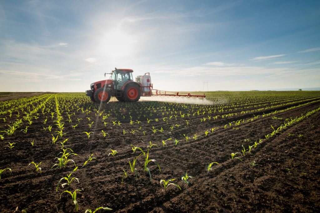 tractor spraying herbice on a corn crop illustrating the importance of herbicide testing in agriculture and land management