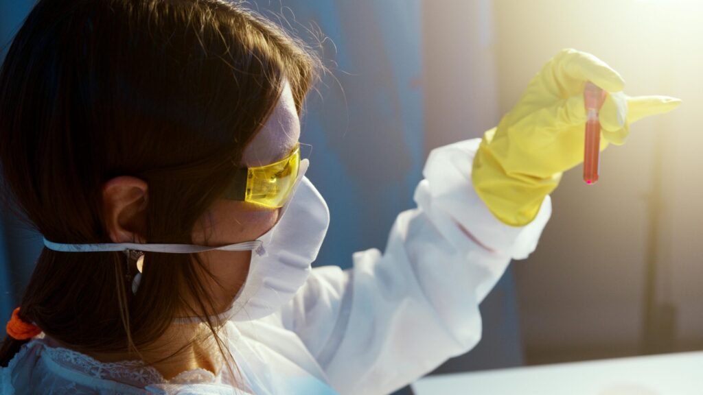 Female researcher wearing PPE examines a test tube filled with liquid.