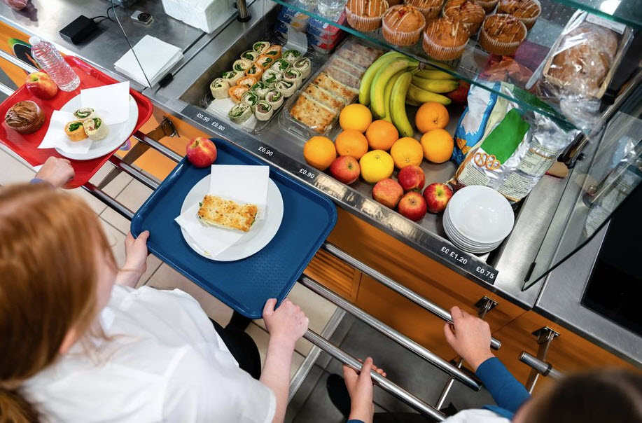 Woman standing at cafeteria line in front of a selection of fresh foods