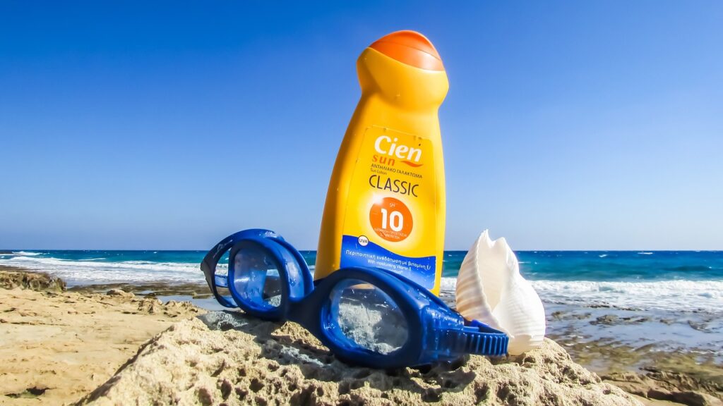 Bottle of sunscreen on sandy beach with goggles and seashell