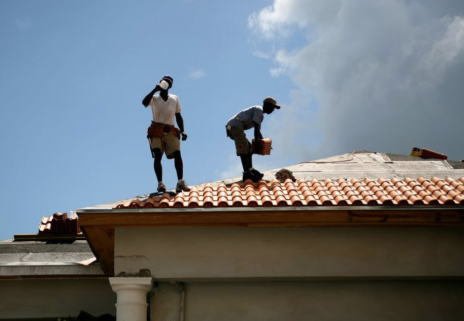 two workers working outdoors on a rooftop on a hot sunny day.