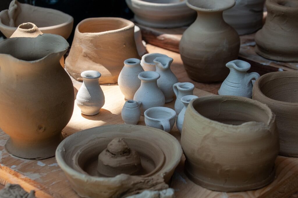 Assorted handmade ceramic pots and miniature vases in various stages of drying, displayed on a wooden surface.
