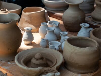 Assorted handmade ceramic pots and miniature vases in various stages of drying, displayed on a wooden surface.