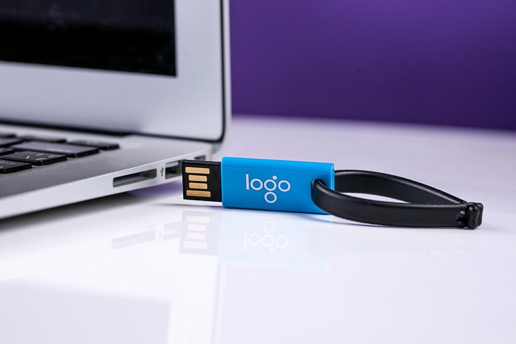 Close-up of a blue USB flash drive with a keyring partially inserted into a silver laptop, symbolizing data storage, transfer, and compliance practices.