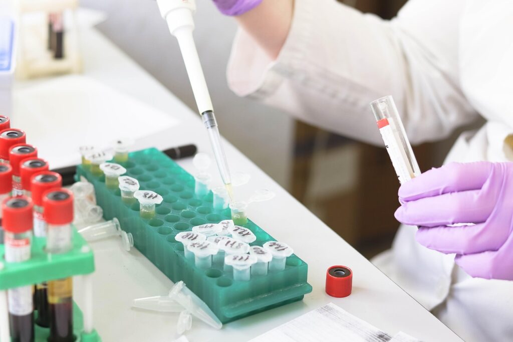Scientist using a pipette to transfer liquid into labeled microcentrifuge tubes at a laboratory workstation.