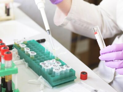 Scientist using a pipette to transfer liquid into labeled microcentrifuge tubes at a laboratory workstation.