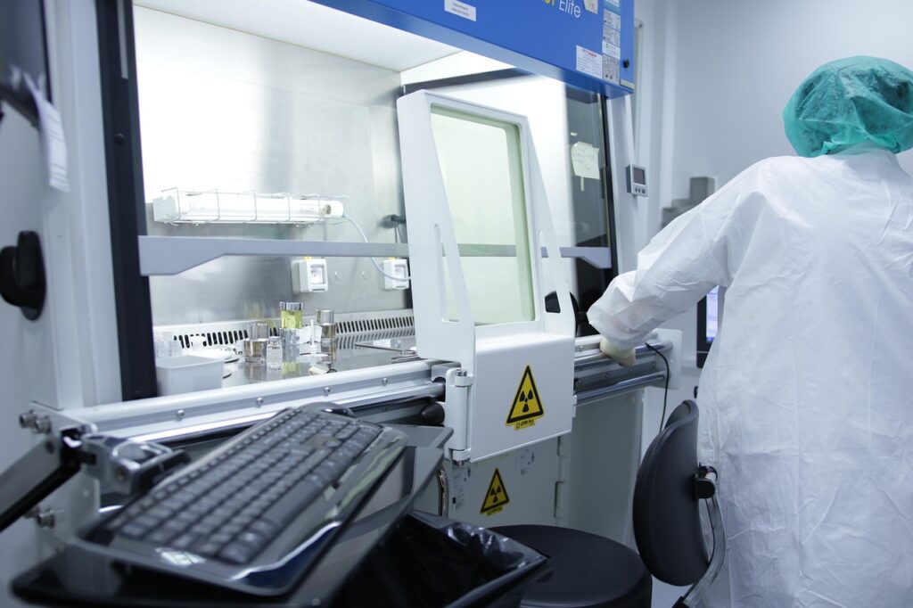 Pharmaceutical professional in cleanroom attire working at a sterile containment unit with biohazard signage, preparing or inspecting equipment for contamination control.
