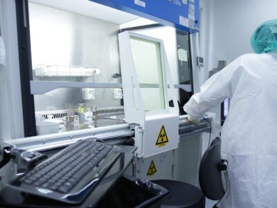 Pharmaceutical professional in cleanroom attire working at a sterile containment unit with biohazard signage, preparing or inspecting equipment for contamination control.