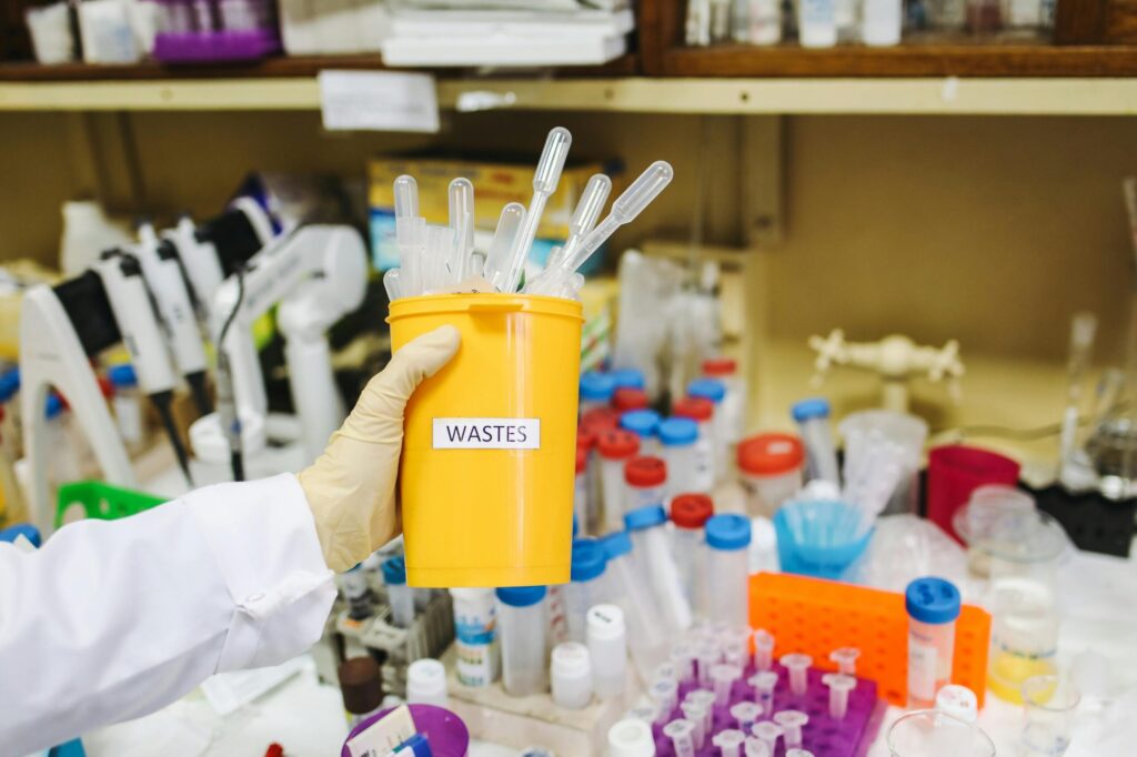 Researcher's gloves hand holding medical waste disposal container.