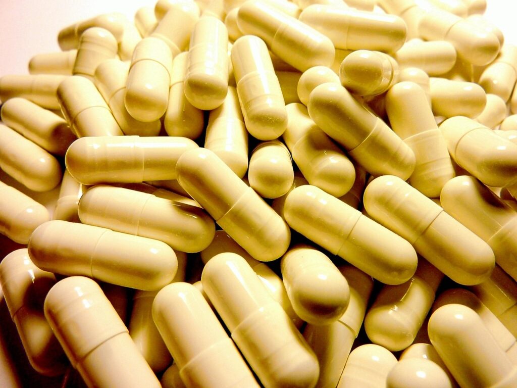 A large pile of beige or off-white pharmaceutical capsules filling the frame.