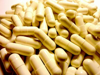 A large pile of beige or off-white pharmaceutical capsules filling the frame.